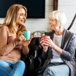 Smiling,Mature,Mother,And,Adult,Daughter,On,Sofa,In,Living