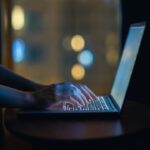 Cropped shot of woman's hand typing on computer keyboard in the dark, working late on laptop at home